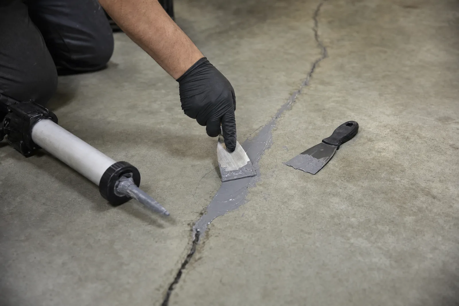 Gloved hand troweling polyurea filler into a routed crack