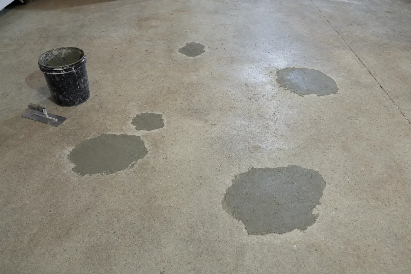 Bare concrete surface with several spalled areas patched with fresh grey repair mortar